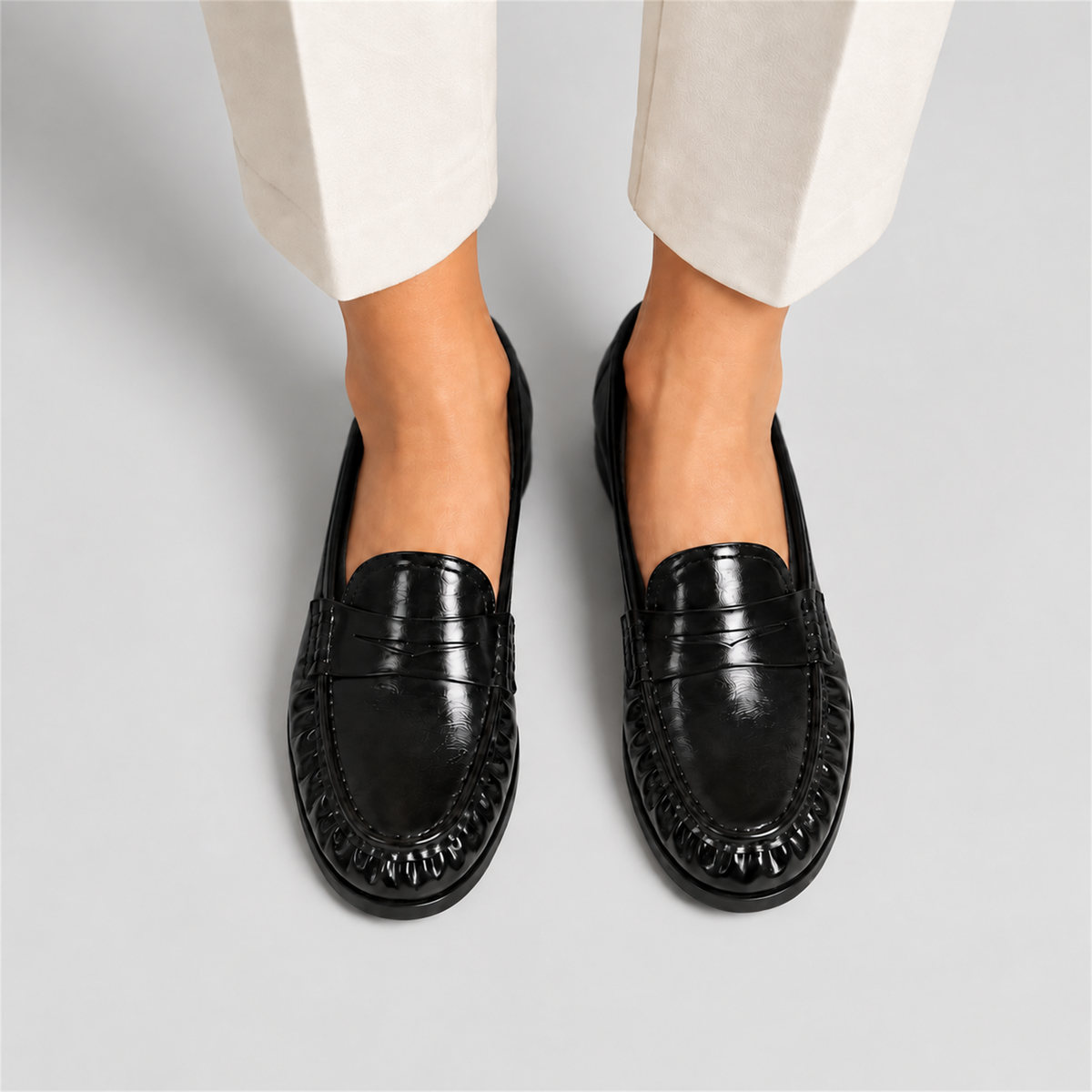 Meta title: Mocassins noirs vernis femme portés - fond studio gris | Meta description: Mocassins noirs vernis portés avec pantalon clair sur fond studio gris, intérieur noir, bride penny et fronces avant pour une allure élégante premium.
